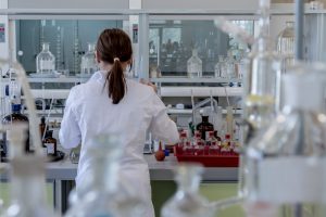 Woman standing in a research lab wearing a white coat with her back to the camera.